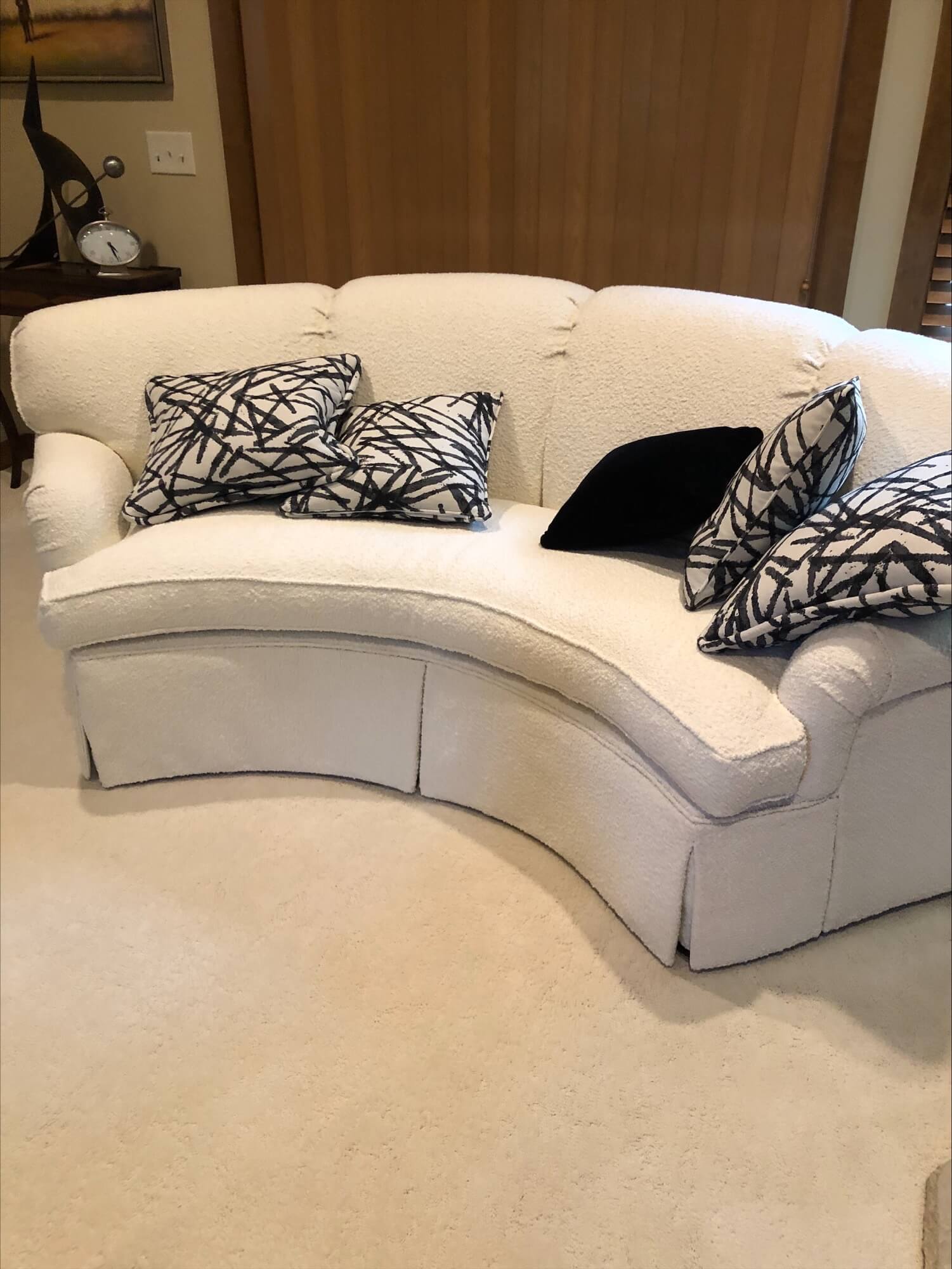 Curved white couch adorned with patterned black and white pillows, situated in a cozy living room setting. Soft textiles enhance comfort.